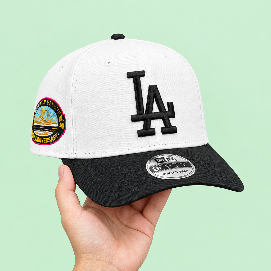White cap with black brim and raised embroidery held in one hand, left three-quarter view on pastel mint-green background