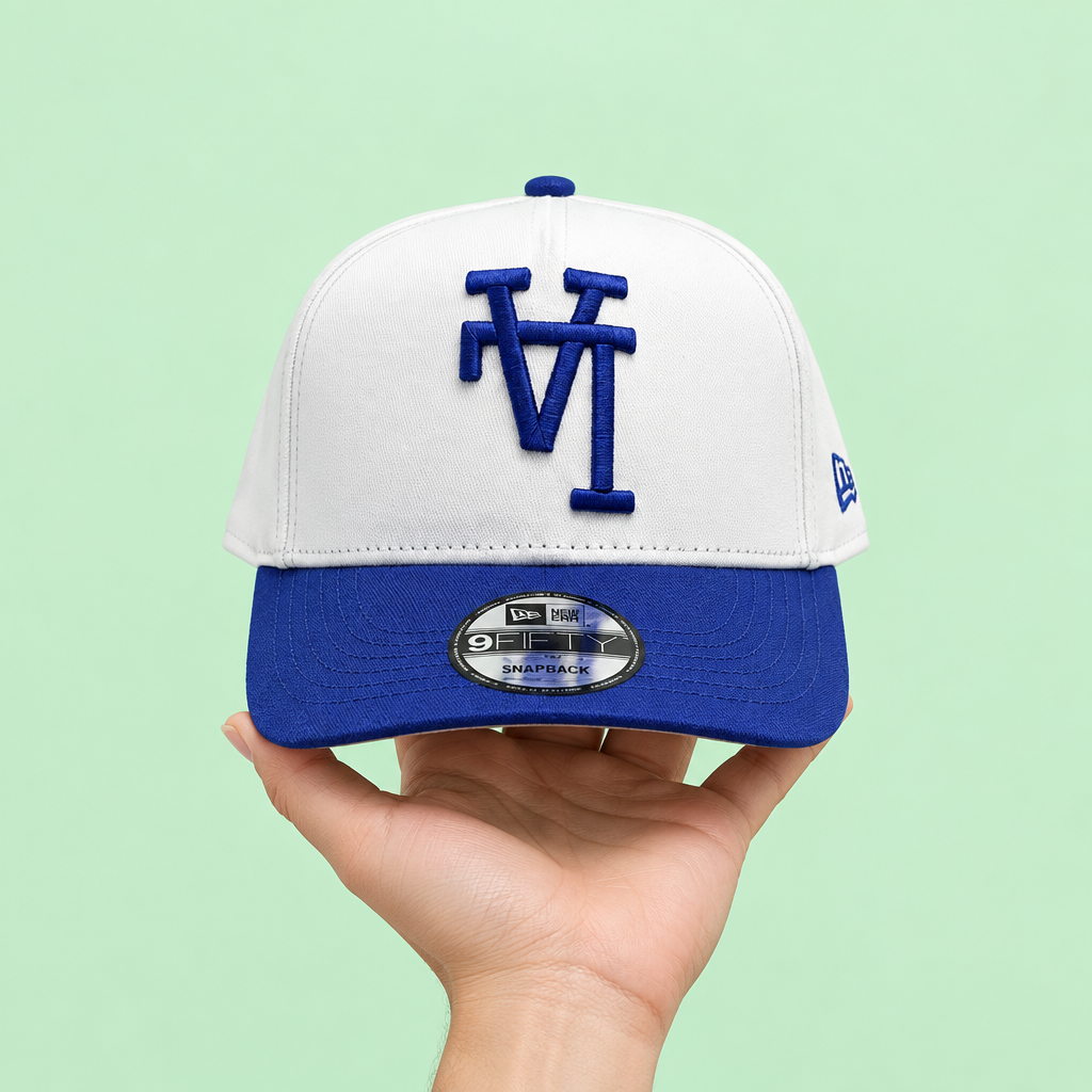 White cap with blue brim held in one hand, front view on pastel mint background