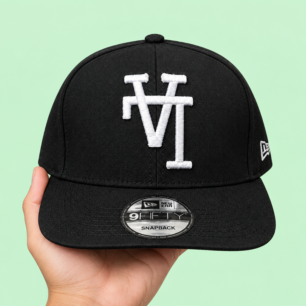 Black snapback cap with white embroidery held in hand, elevated front view