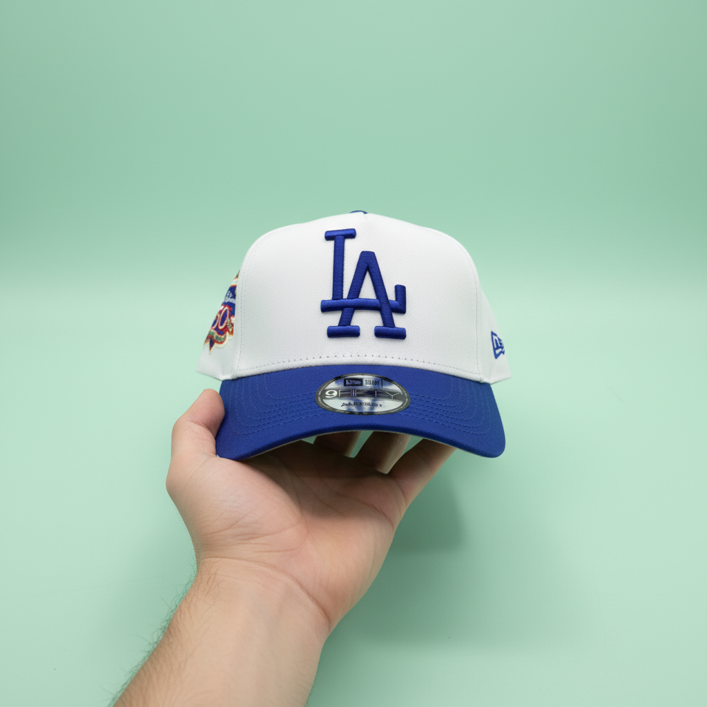 White and blue embroidered baseball cap held by hand from an elevated top-front angle on a pastel mint green background