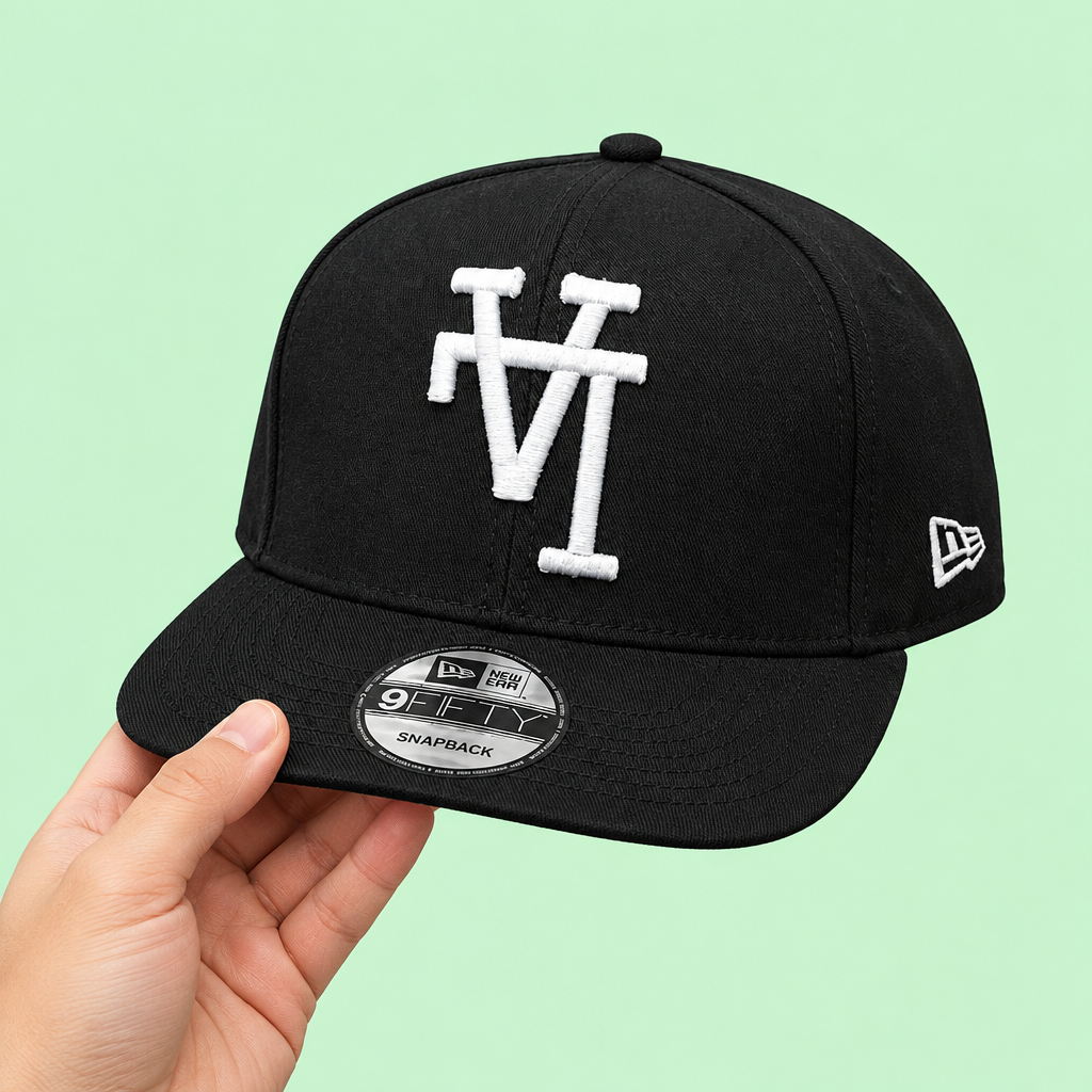 Black snapback cap with white embroidery held in hand, three-quarter view